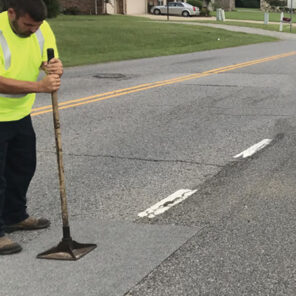 Image of man holding down an American Road Patch seal over the asphalt pothole repair.